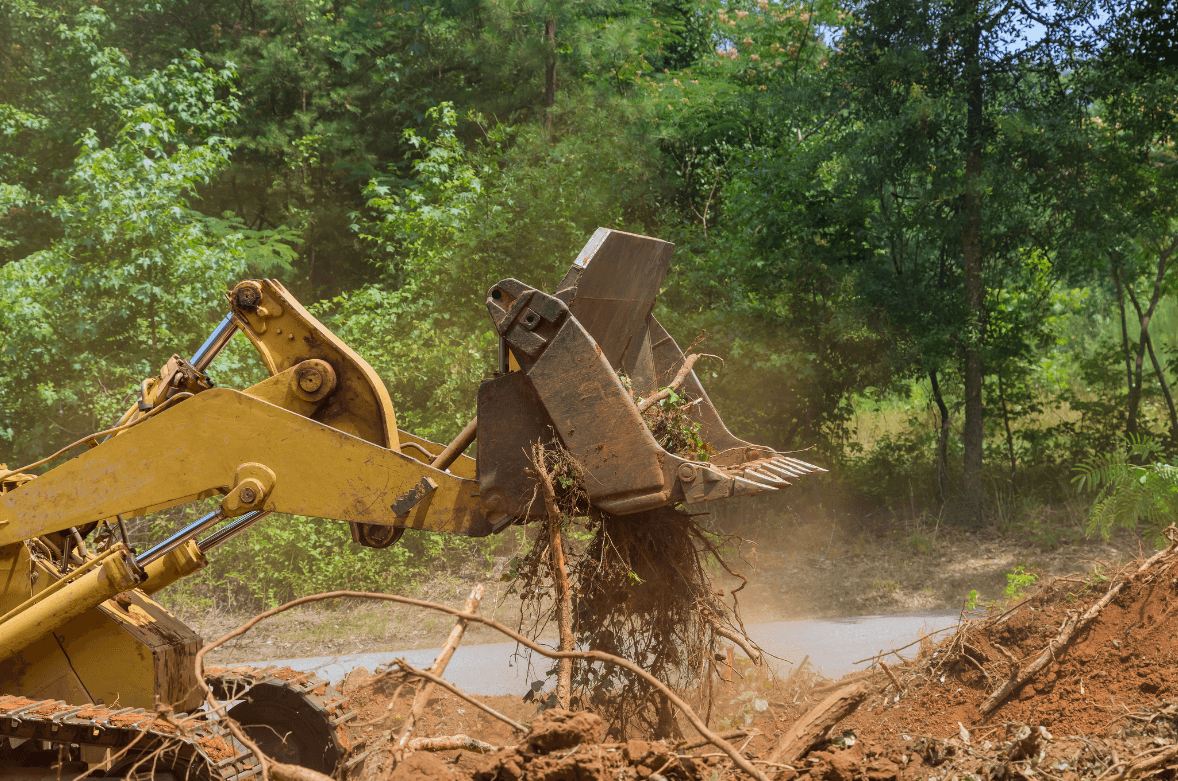 a yellow tractor clearing away debris on a lot of land